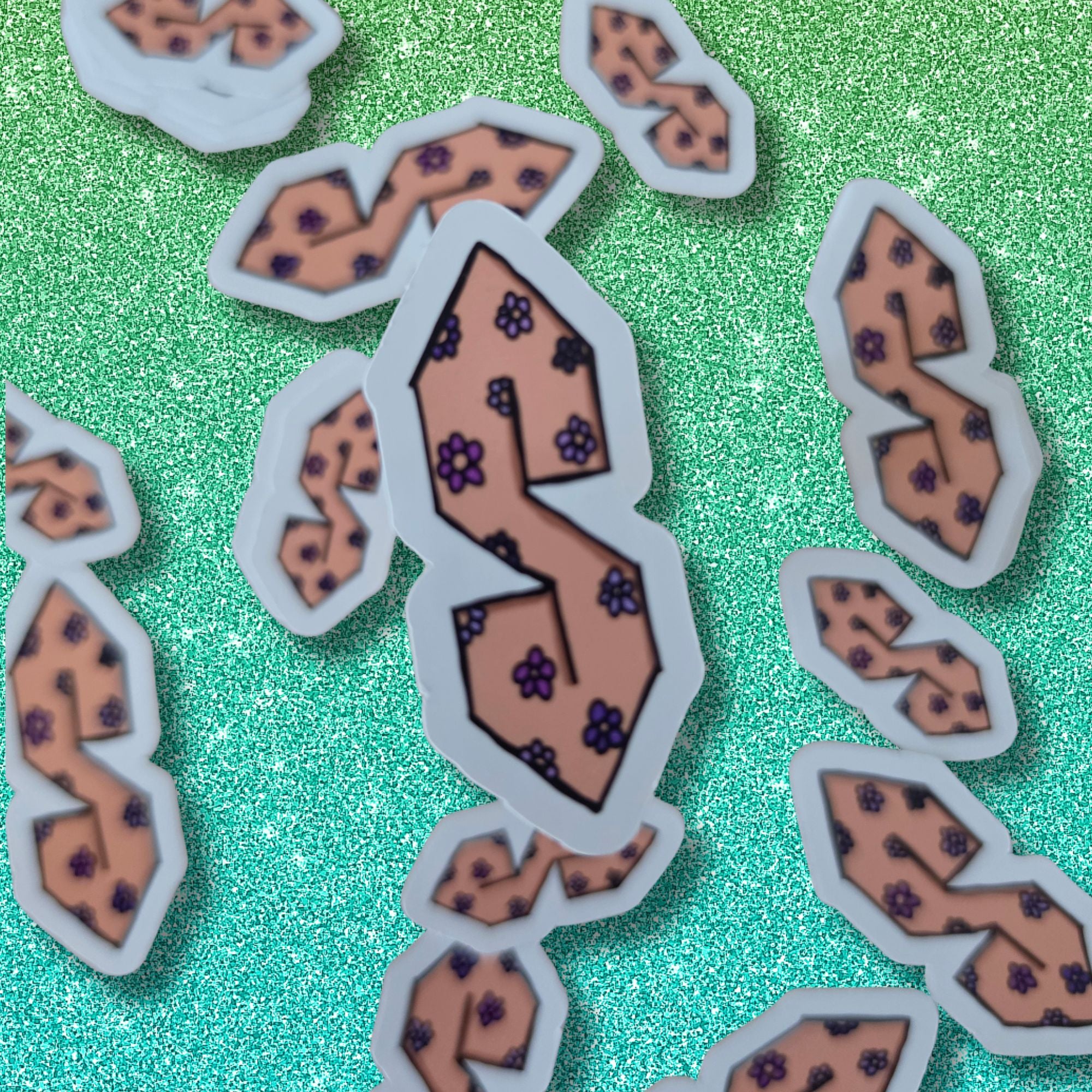 A collection of die-cut stickers featuring a stylized peach-colored letter 'S' decorated with small purple flowers, arranged on a sparkling teal-green background.