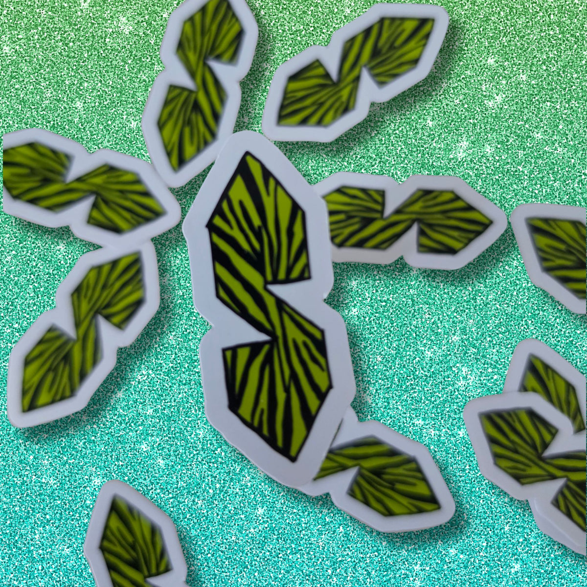 A set of die-cut stickers featuring a stylized green and black striped letter 'S' on a white border, arranged on a sparkling teal background.