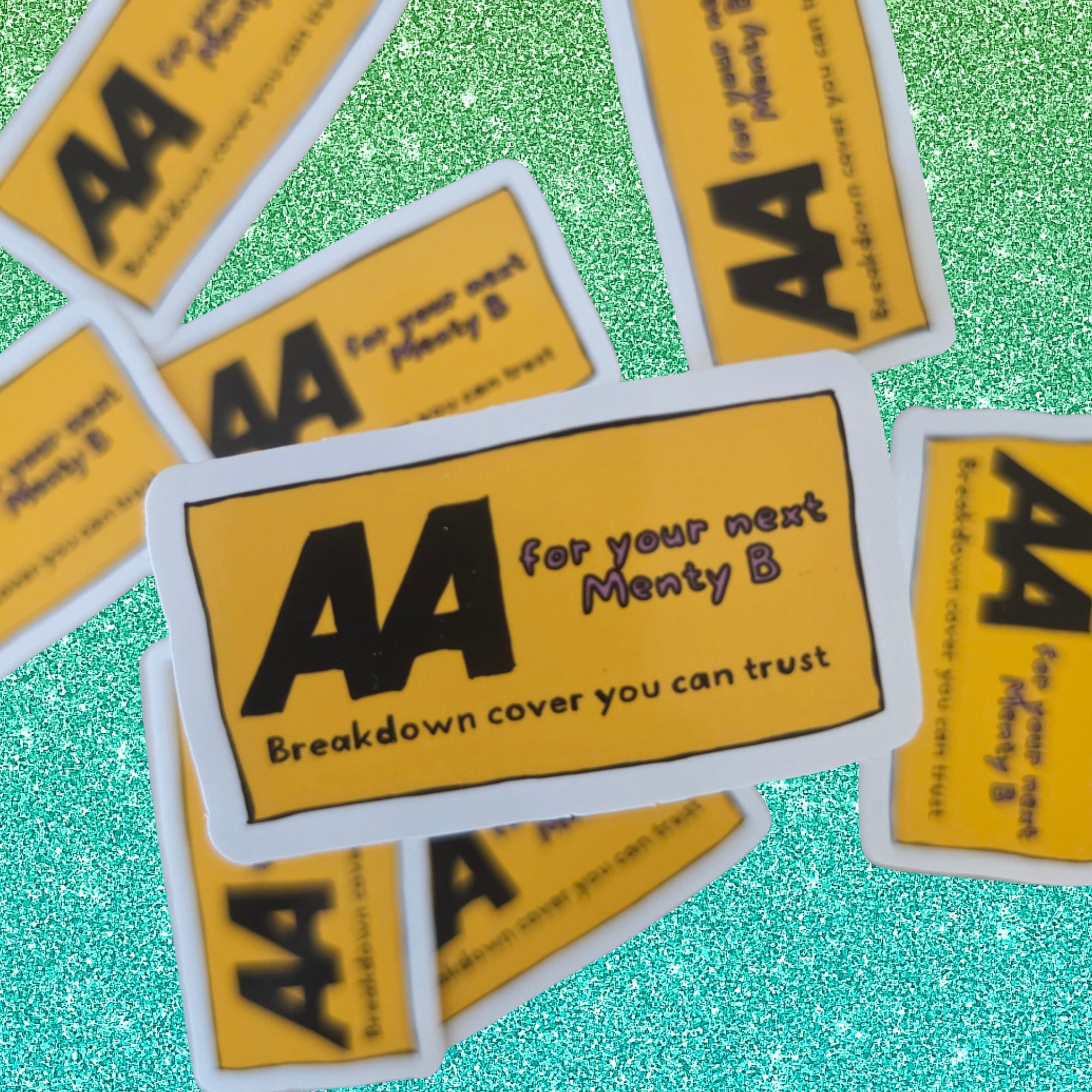 Multiple AA recovery stickers are scattered on a glittery teal background. The central sticker is clearly shown with a white border, yellow background, and black text reading 'AA for your next Menty B Breakdown cover you can trust'.