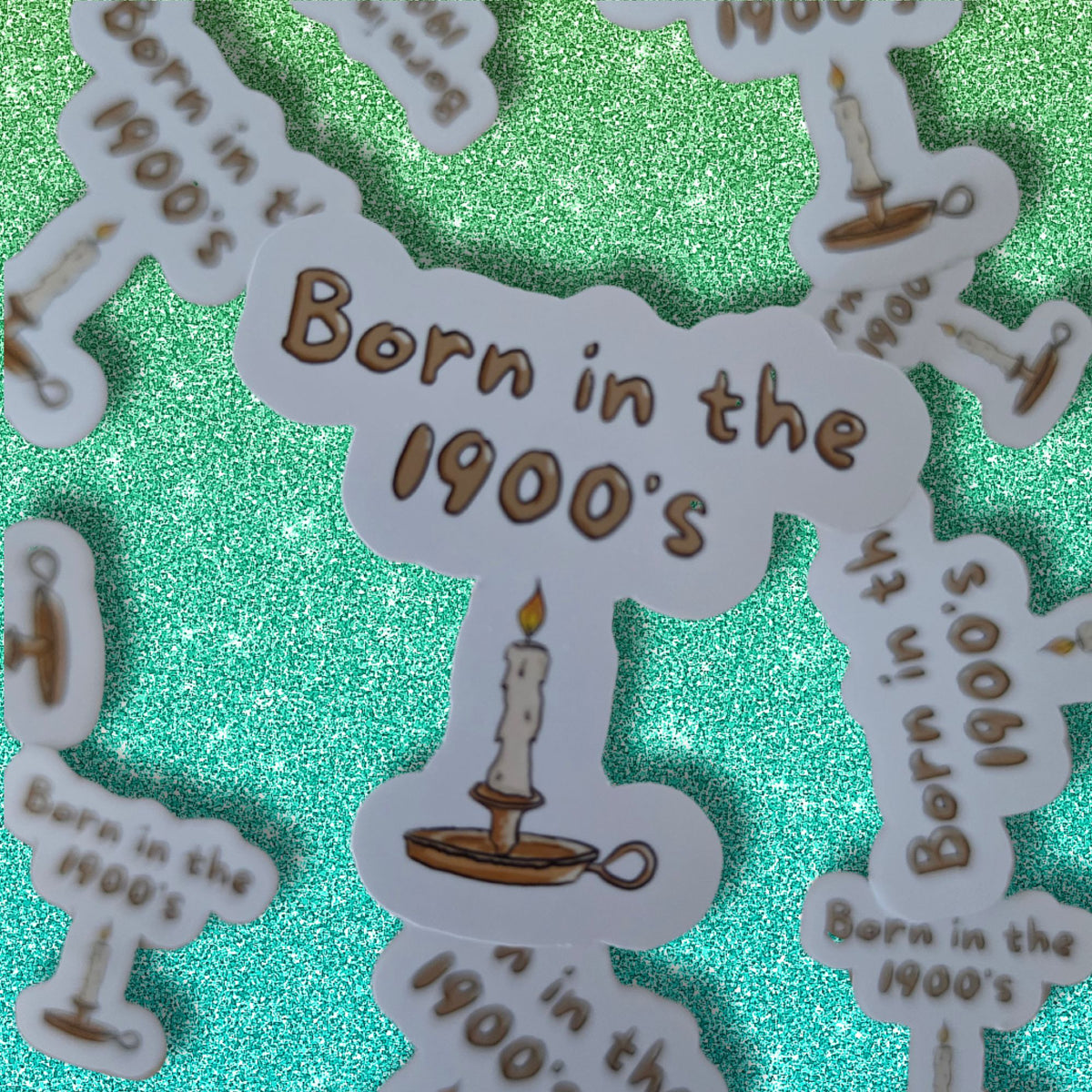 White die-cut stickers with the text 'Born in the 1900's' in brown, each illustrated with a single candle on a stand, arranged on a sparkling teal-green background.