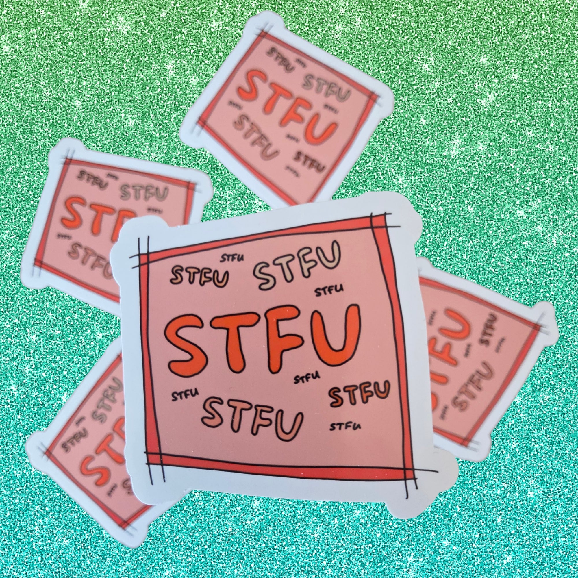 Several die-cut stickers with a pink and orange design featuring the word 'STFU' are arranged on a glittery green background.