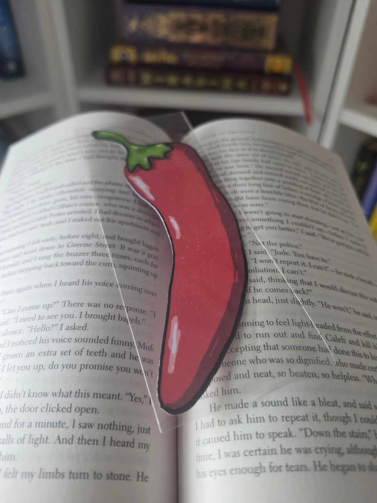 A glossy red chili pepper bookmark with a green stem, laid on the page of an open book.