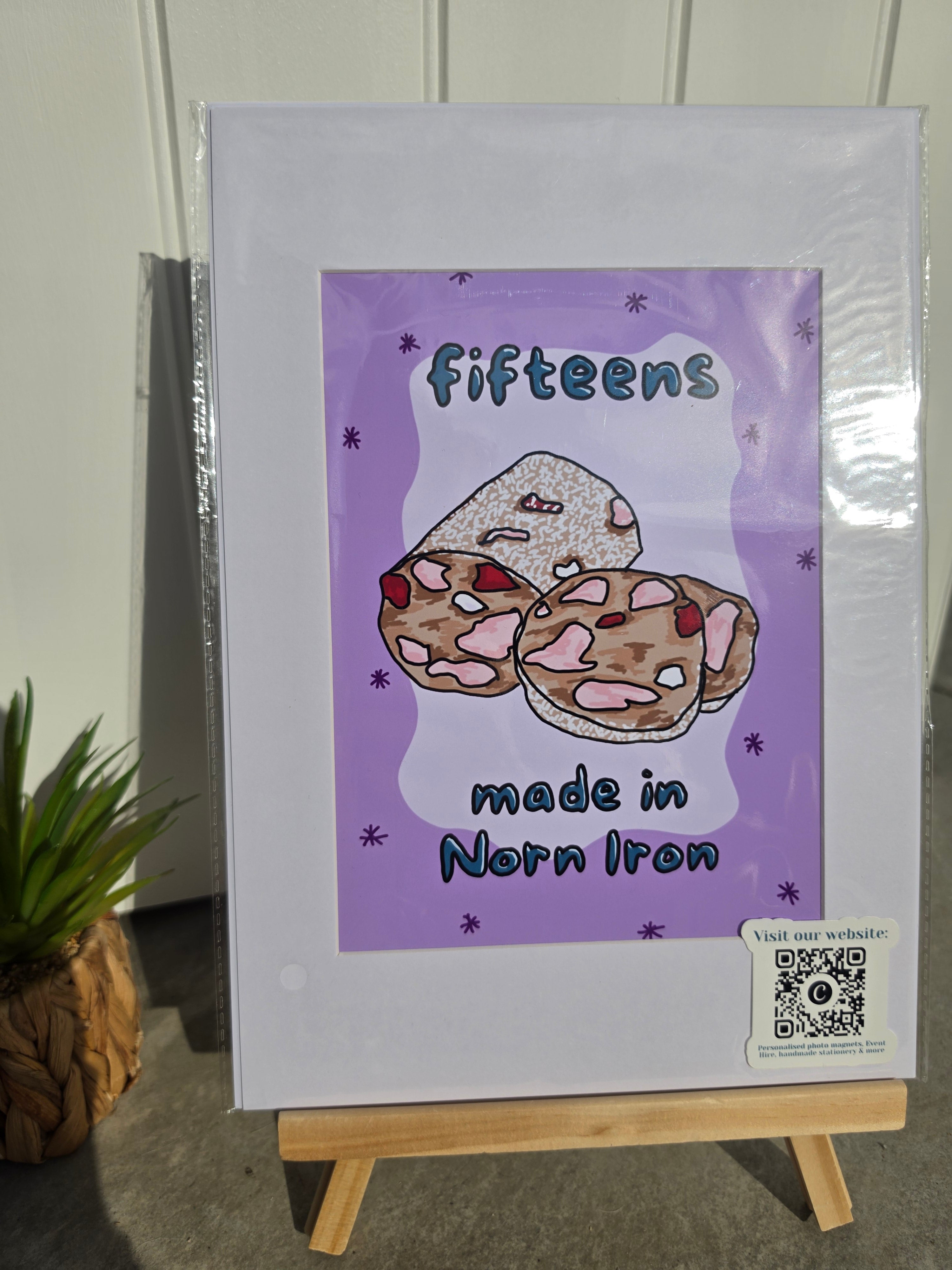 A framed or mounted art print displayed on a small wooden easel, featuring a purple background with the words 'fifteens made in Norn Iron' and an illustration of three decorated cookies. 