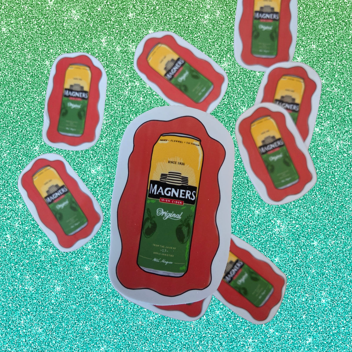 A set of die-cut stickers shaped like vintage Magners cider arranged on a sparkling green background. The central sticker is upright and clearly shows the yellow and green label with red borders, while other stickers are scattered around it.