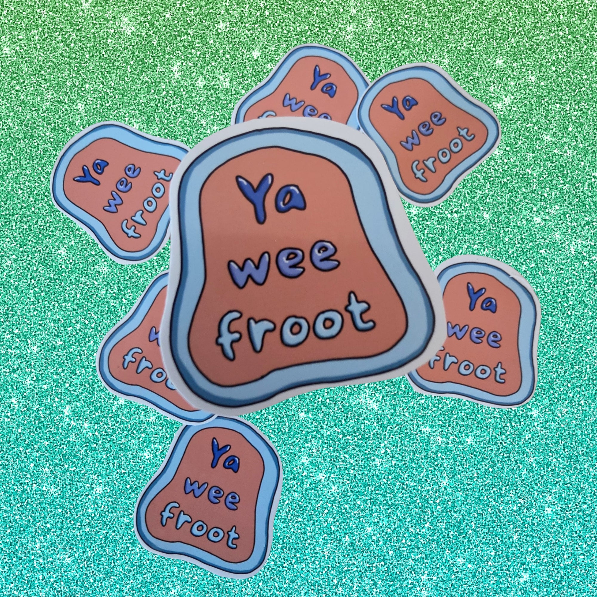 A set of die-cut stickers featuring the phrase 'Ya wee froot' in blue lettering on a peach-orange background, surrounded by a light blue border. The main sticker is in the center, with six smaller matching stickers arranged around it on a sparkling teal background.