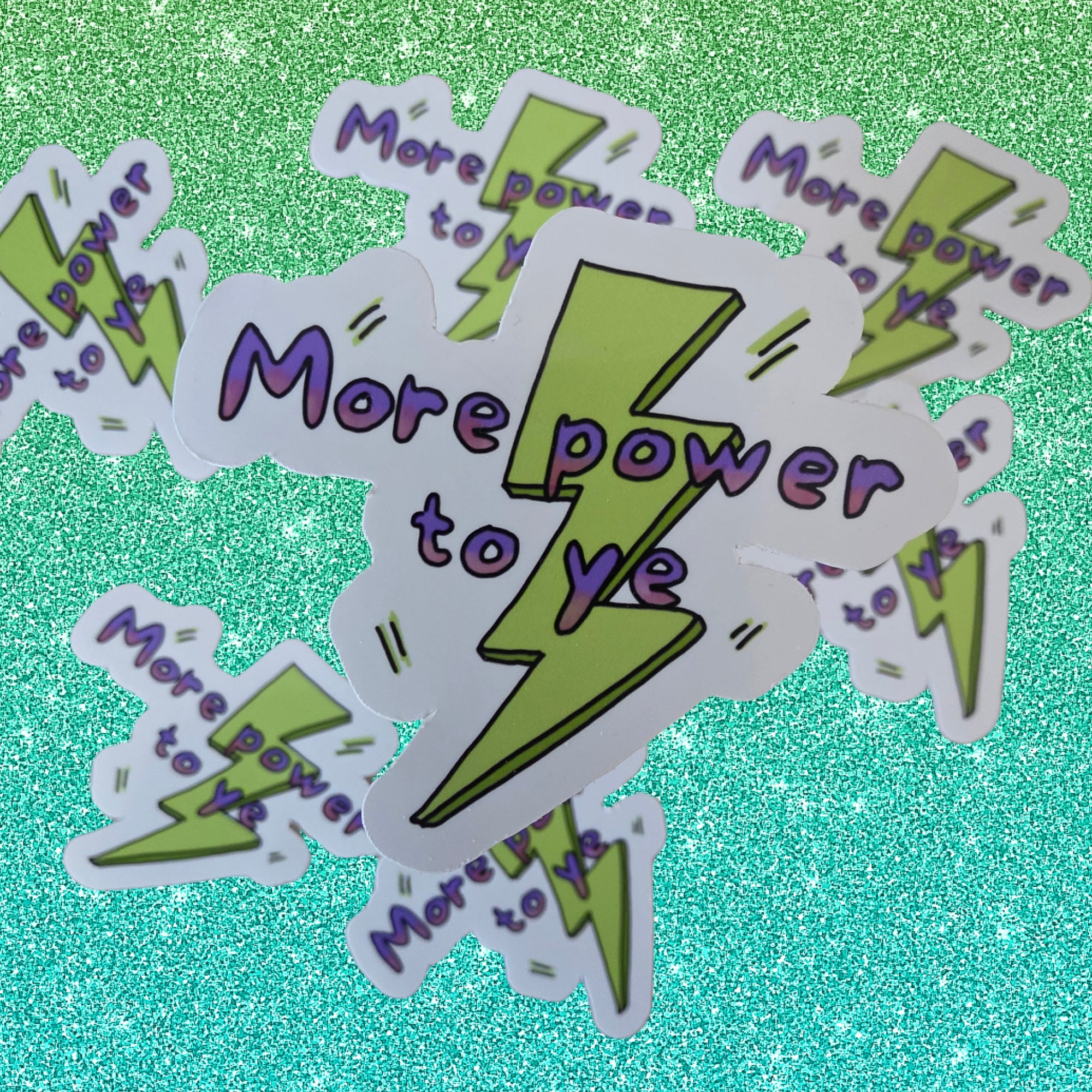 A pile of white die-cut stickers featuring a lime green lightning bolt and the text 'More power to ye' in purple, set against a sparkling teal background.