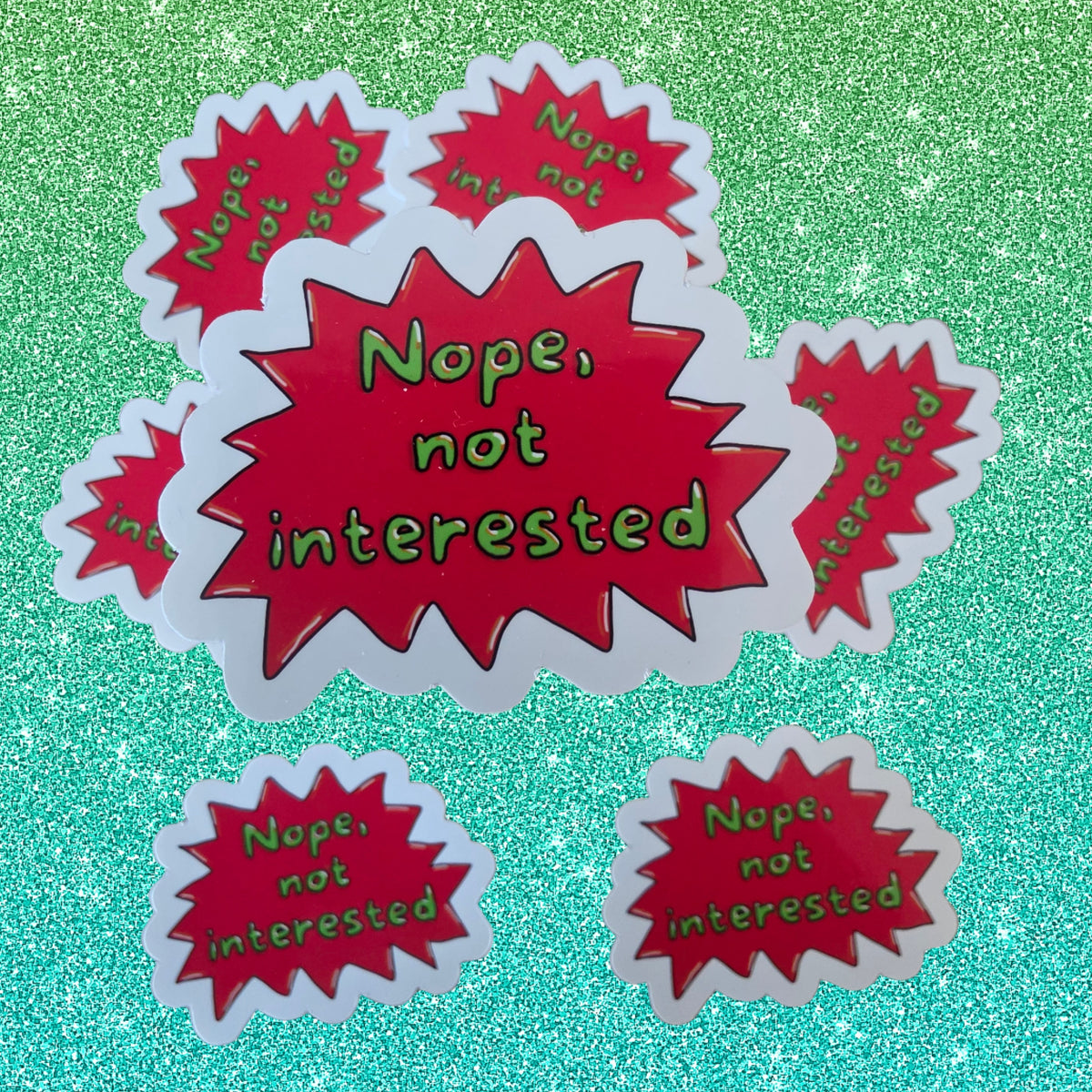 A set of die-cut stickers featuring a red starburst design with the text 'Nope, not interested' in green lettering, displayed on a sparkling green background.