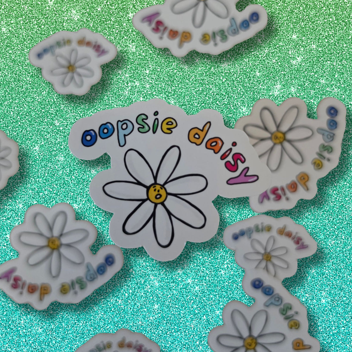 A collection of die-cut stickers featuring a daisy flower and the text 'oopsie daisy' in colorful lettering, arranged on a sparkling mint green background.