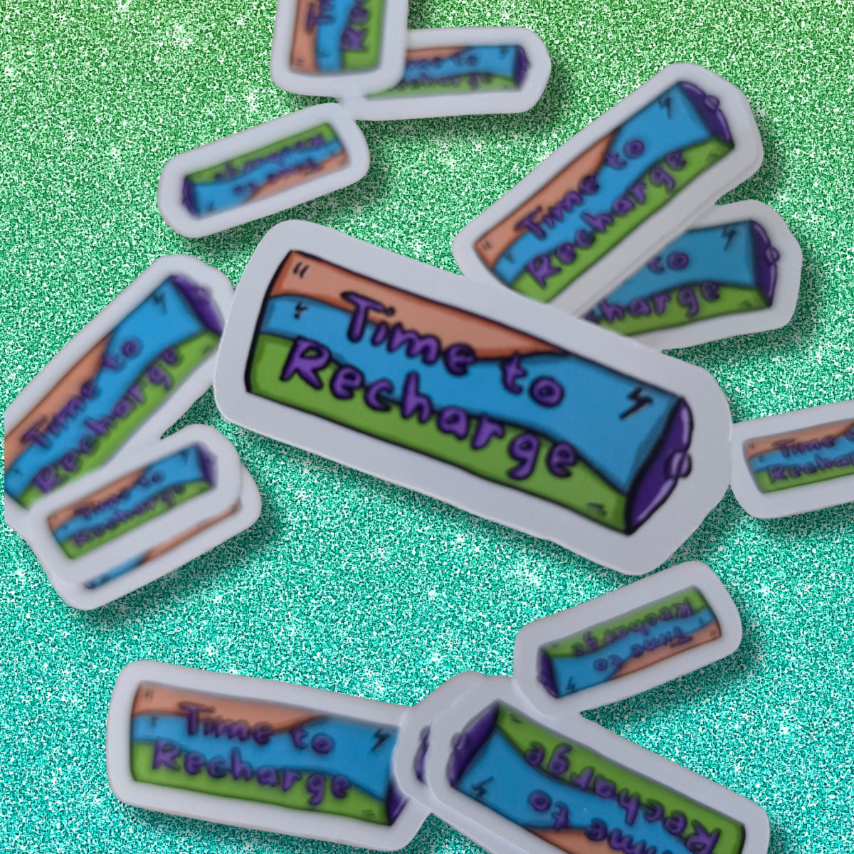 Several small battery shaped stickers scattered on a glittery turquoise background. Each sticker shows a battery illustration and the phrase “Time to Recharge” in purple text